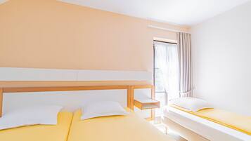 Hotellihuone, jossa on kaksi sänkyä, puinen pääty ja ikkuna, jossa on verhot.