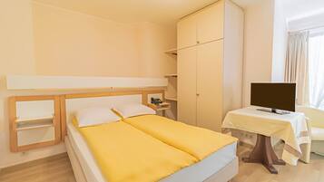 A hotel room with a double bed, a wardrobe, a bedside table with a lamp, and a TV.