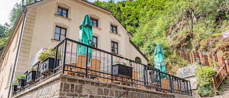 A building with a stone staircase leading to a balcony with outdoor seating and umbrellas.
