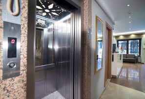 An elevator with a digital display, a granite wall, and a reception area with a sofa and a window.