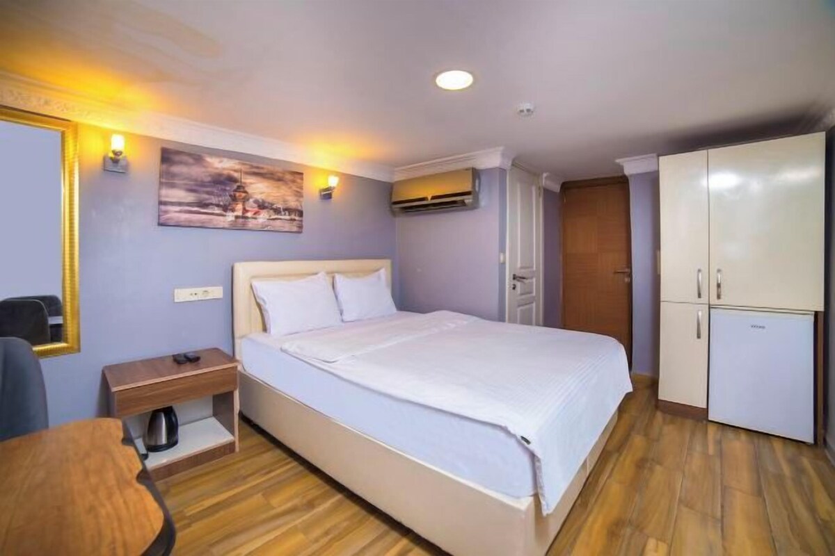 Habitación de hotel con cama, mesita de noche, silla, armario y un cuadro en la pared.
