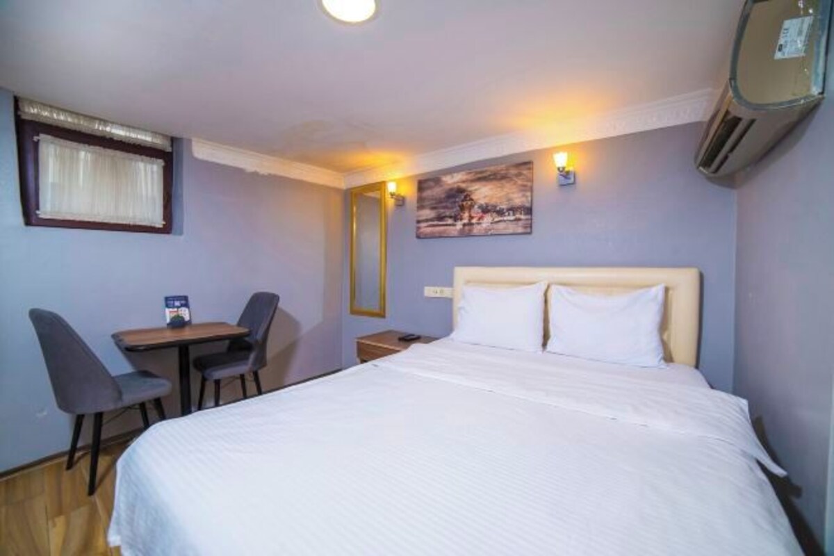 Una camera d'albergo con un letto, una scrivania, due sedie, un comodino e un condizionatore d'aria a parete.
