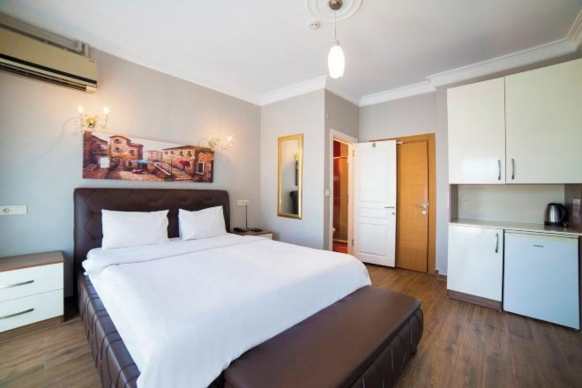 Una camera da letto con un letto, comodini, un angolo notte, un quadro, uno specchio, un armadio e un angolo cottura.