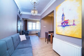 A modern living room with a grey sofa, a dining area with a table and chairs, and a large painting on the wall.