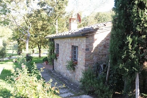 Una casa de piedra con tejado de tejas, chimenea y un pequeño jardín con plantas en macetas.