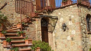 A stone building with a staircase leading to a wooden balcony, surrounded by potted plants. - Relais San Bruno (Montepulciano)