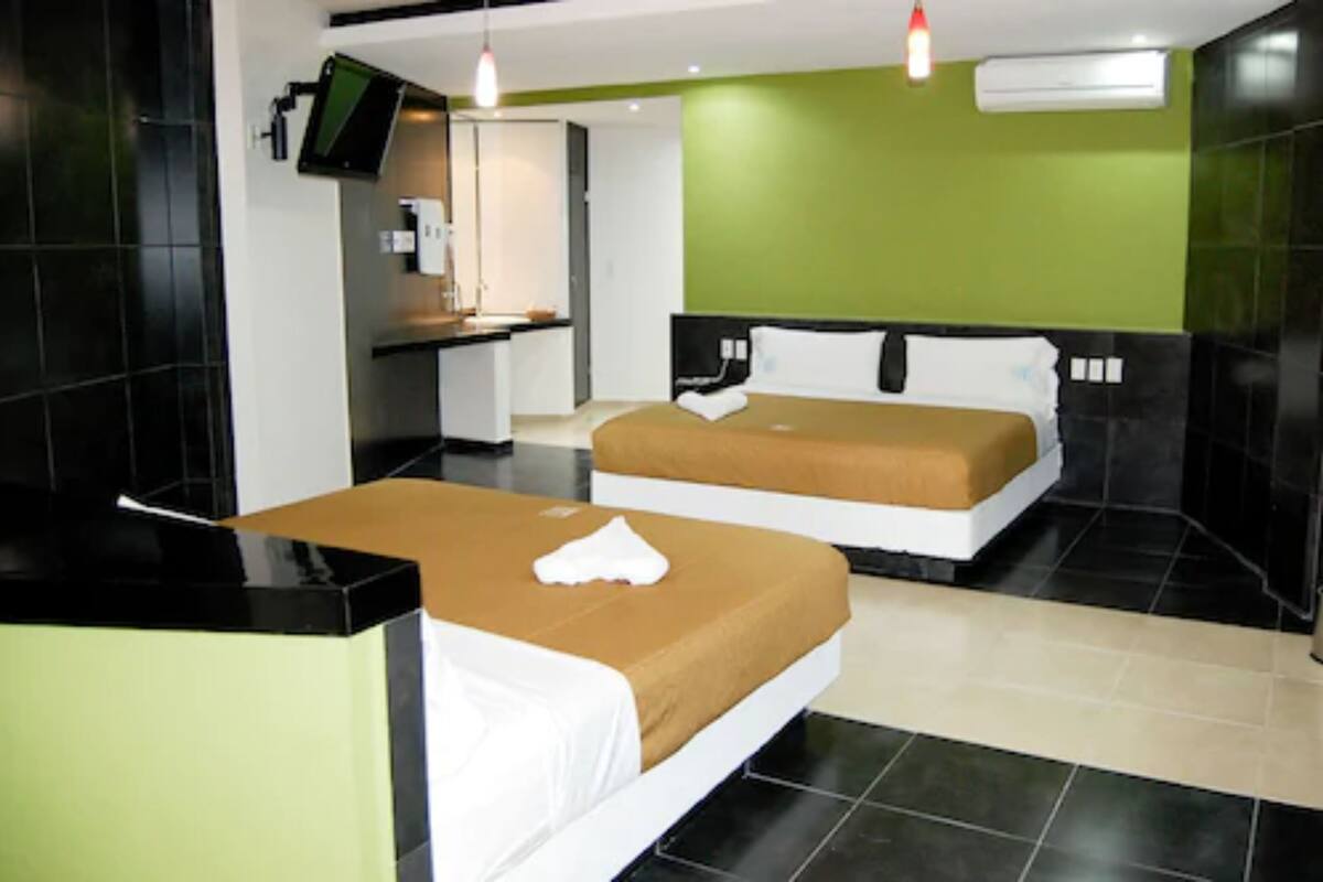 A hotel room with two beds, a desk, a TV, and a green wall.