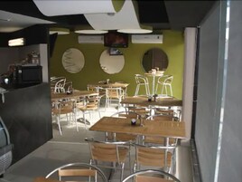Comedor con varias mesas y sillas, televisor y cocina equipada.