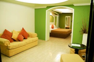 Una habitación con un sofá amarillo, una mesita redonda y una cama al fondo.