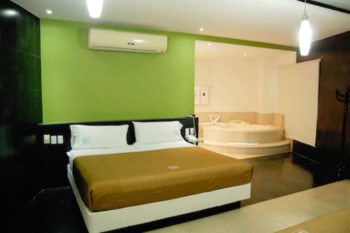 A hotel room with a bed, a bathtub, and a green wall.