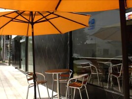 Café con terraza, mesas y sillas, y un amplio paraguas naranja que ofrece sombra.
