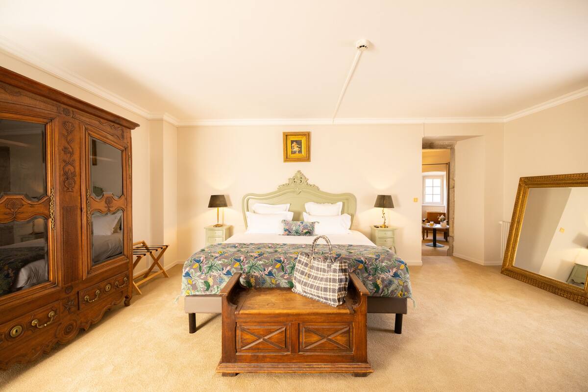 A bedroom with a large wooden wardrobe, a bed with a floral bedspread, and a large mirror.