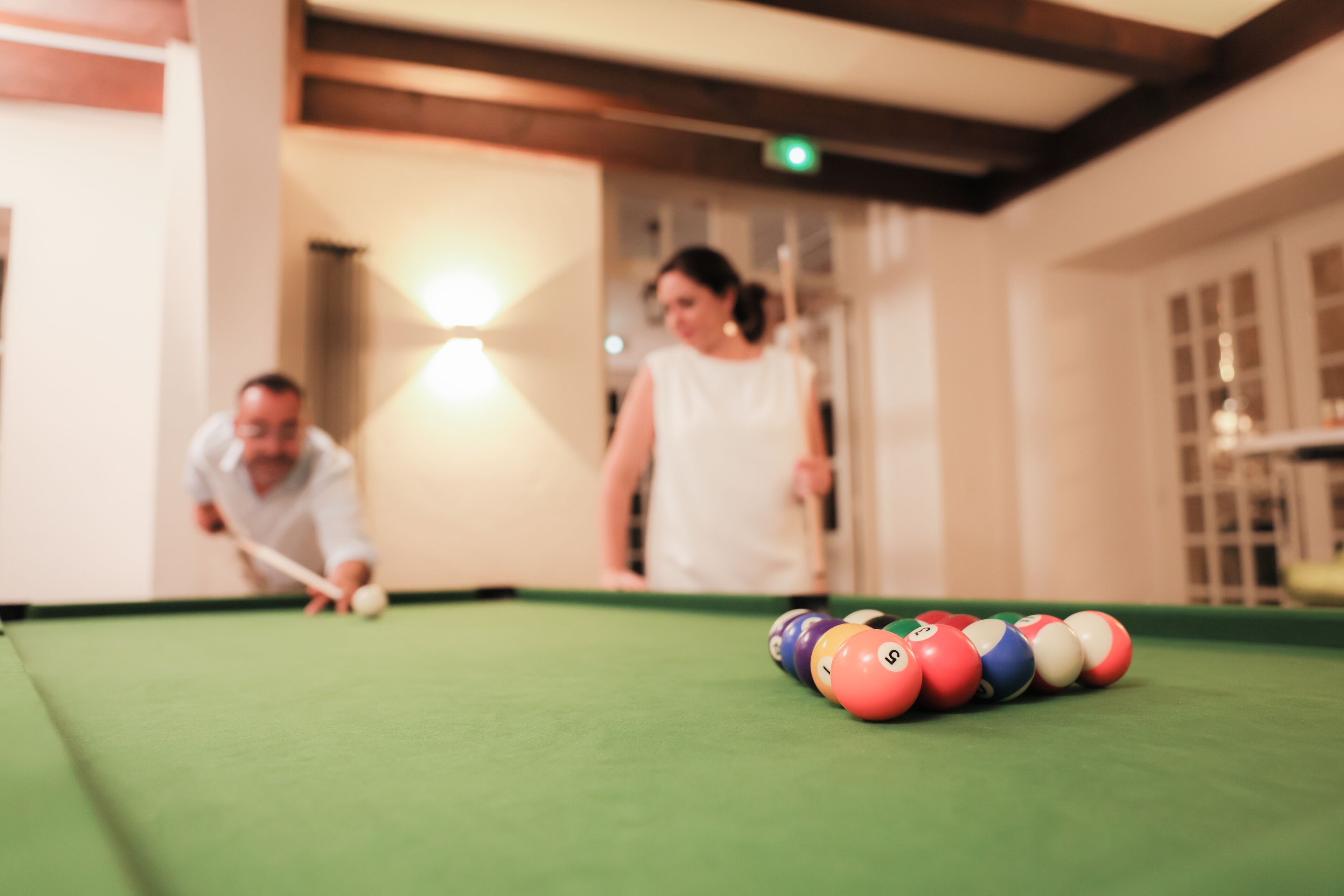 Une table de billard avec des billes, dans une pièce dotée de poutres en bois et d’un luminaire.
