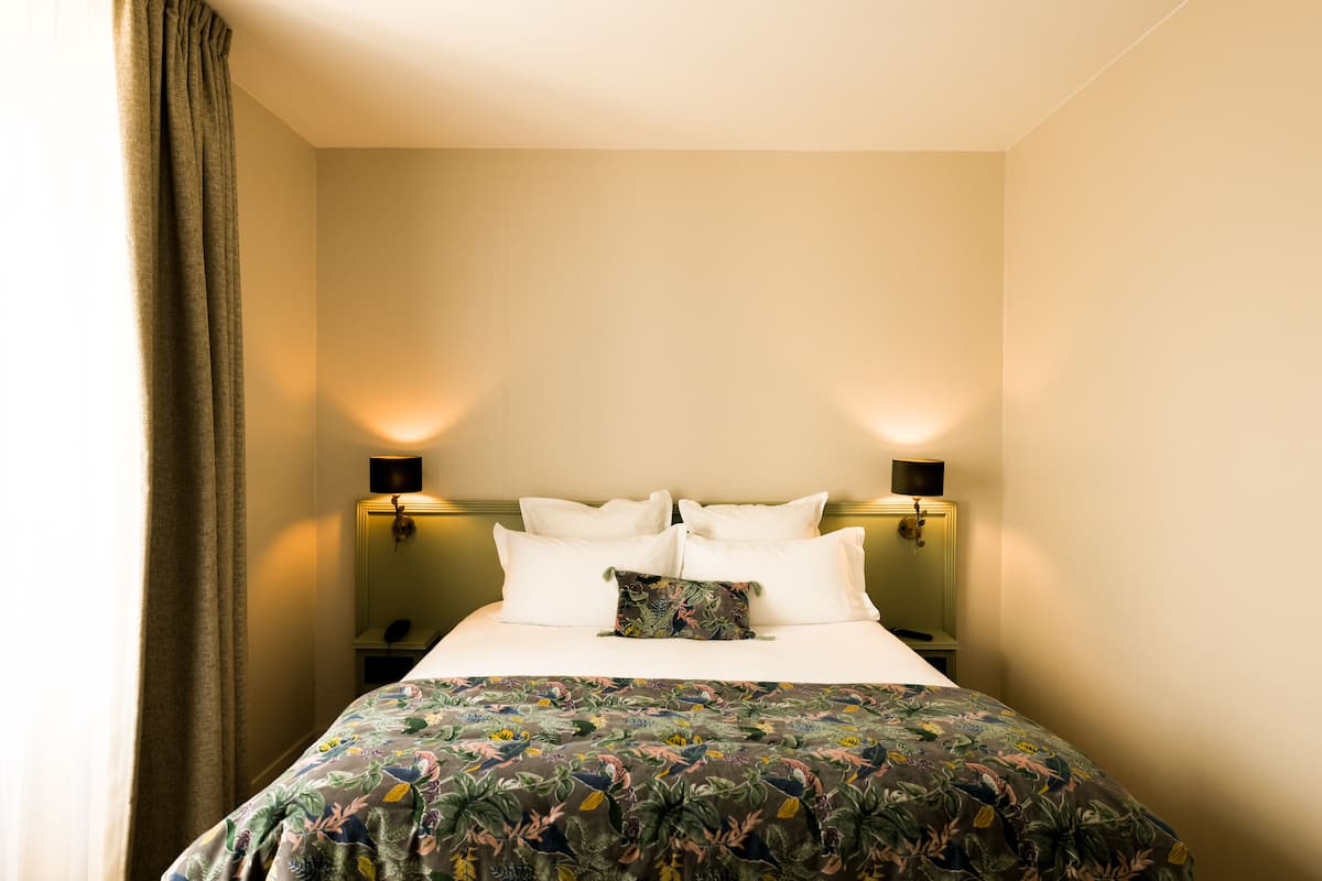 A hotel room with a bed, two bedside tables, a nightstand, and a wall-mounted lamp.