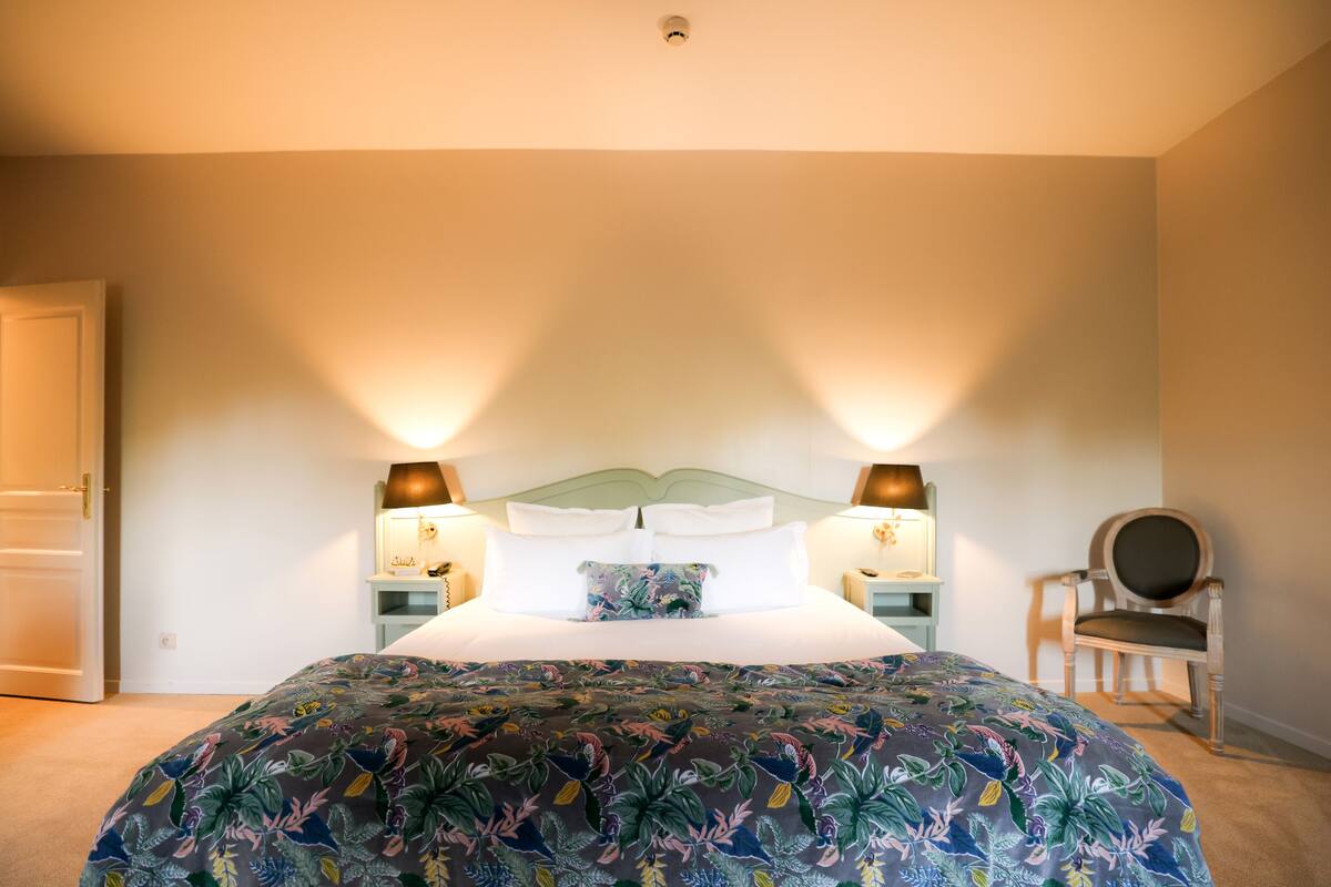 A bedroom with a large bed, two bedside lamps, a chair, and a nightstand.