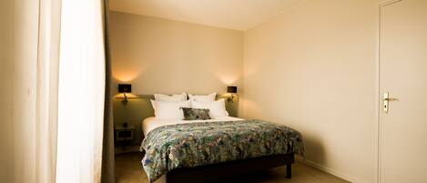A bedroom with a bed, a nightstand, a lamp, and a door.