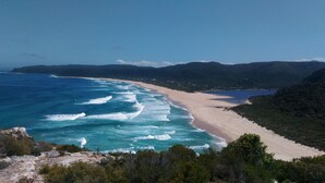 Un paisaje costero con una playa, olas del océano y colinas boscosas.