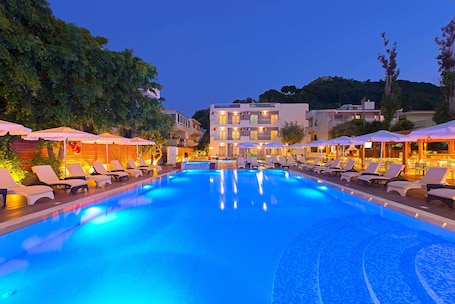 A swimming pool with lounge chairs and umbrellas, surrounded by buildings.