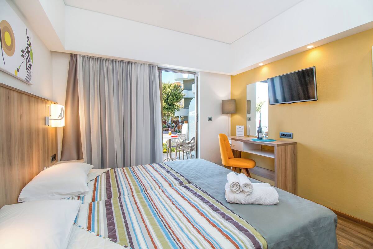 Une chambre d’hôtel équipée d’un lit, d’un bureau, d’une chaise, d’une télévision et offrant une vue sur l’extérieur.