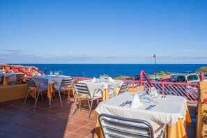 Un área de comedor al aire libre con mesas y sillas, con vistas al mar.