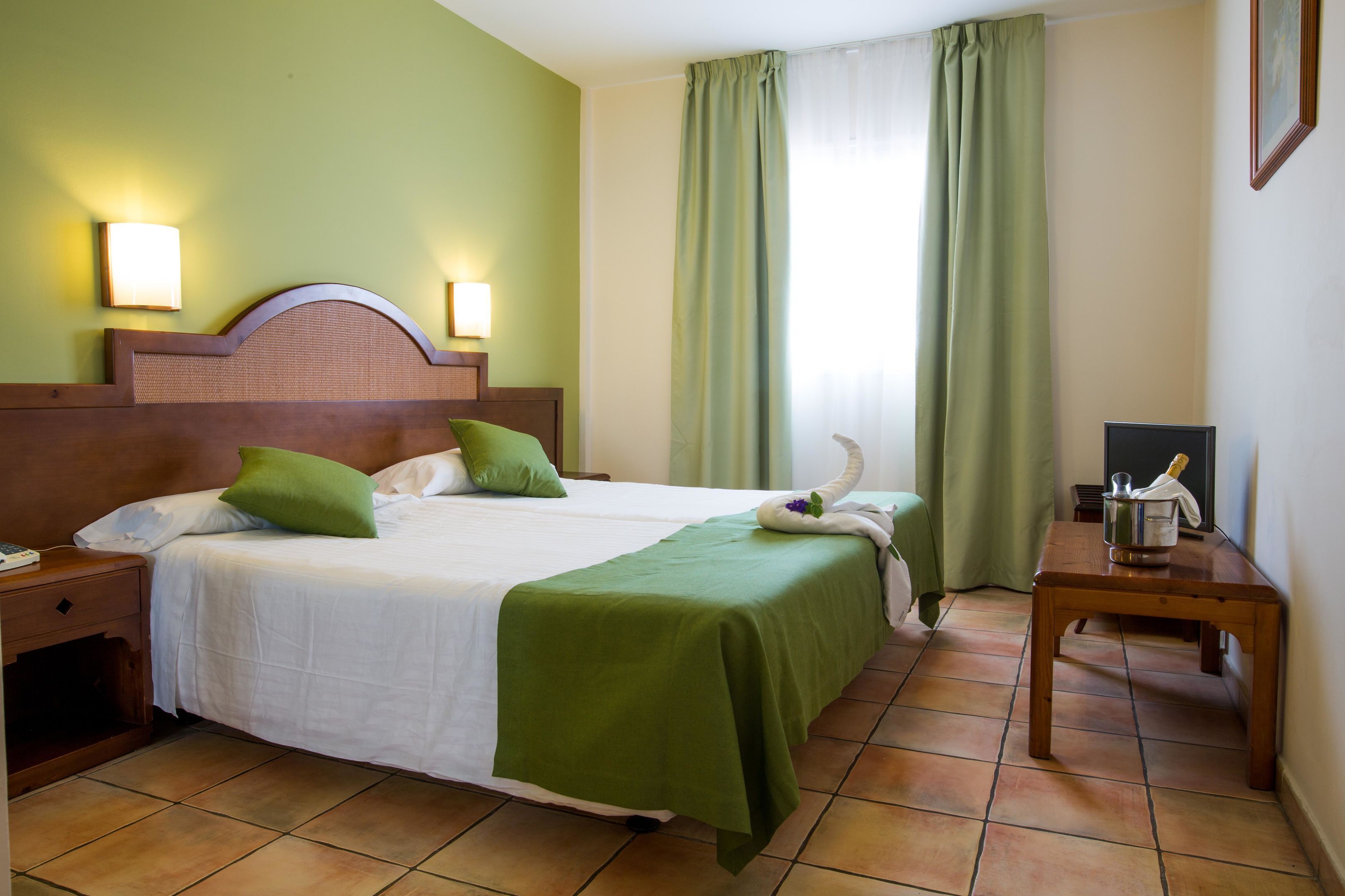 A neatly made bed with green pillows, a wooden headboard, and a bedside table with a lamp.