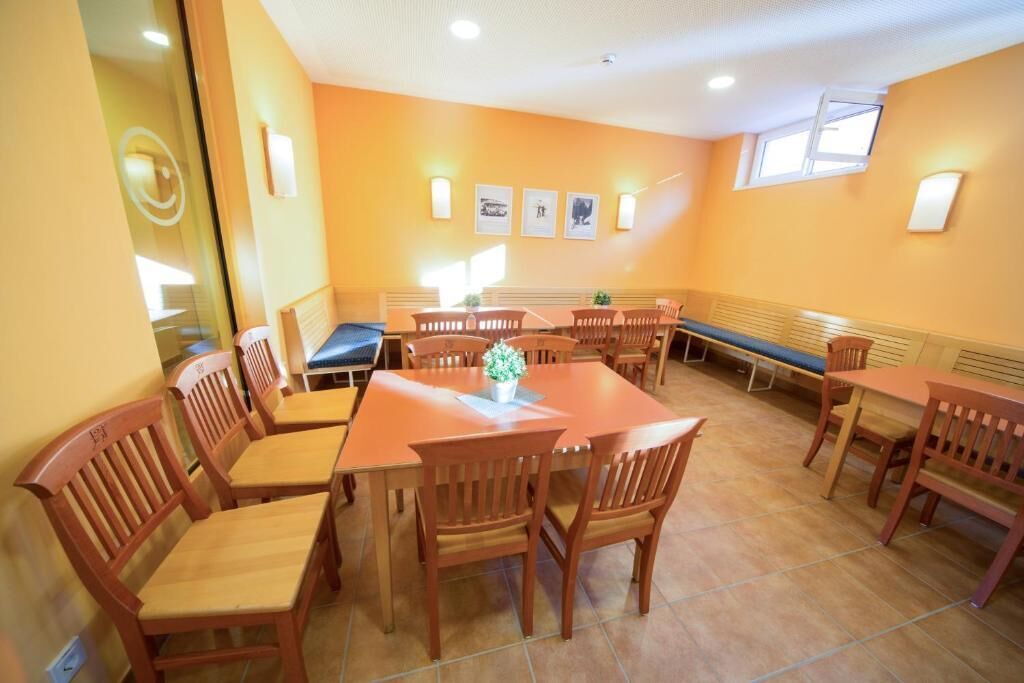 Ein Essbereich mit mehreren Holztischen und -stühlen, einer Sitzbank in der Mitte und Wandleuchten.