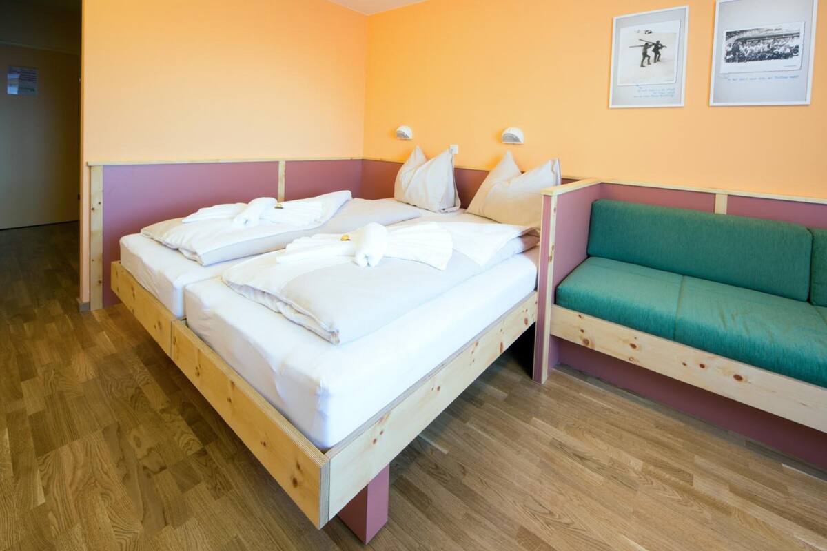 A room with a wooden bed, a green sofa, and two wall-mounted lamps.