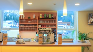 A coffee shop interior with a coffee machine, shelves of glassware, and a view of buildings outside. - JUFA Hotel Planneralm (Irdning-Donnersbachtal)