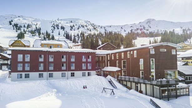 A multi-story building with a red and white facade, situated in a snowy mountainous area with visible ski slopes in the background. - JUFA Hotel Planneralm (Irdning-Donnersbachtal)