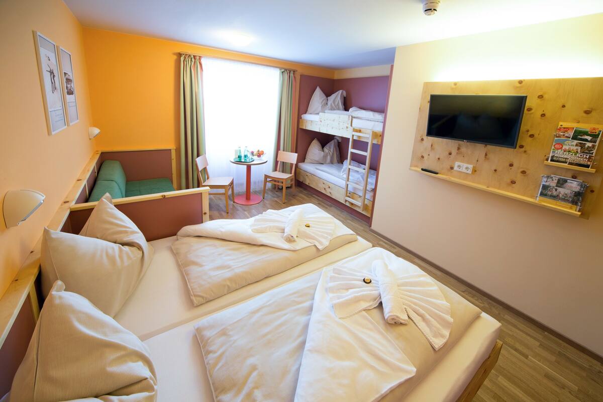 A hotel room with two beds, a TV, a small table, and a green sofa.