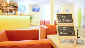 A modern interior with orange seating, a reception desk, and a chalkboard sign welcoming guests to the new JUFA Planneralm. - JUFA Hotel Planneralm (Irdning-Donnersbachtal)