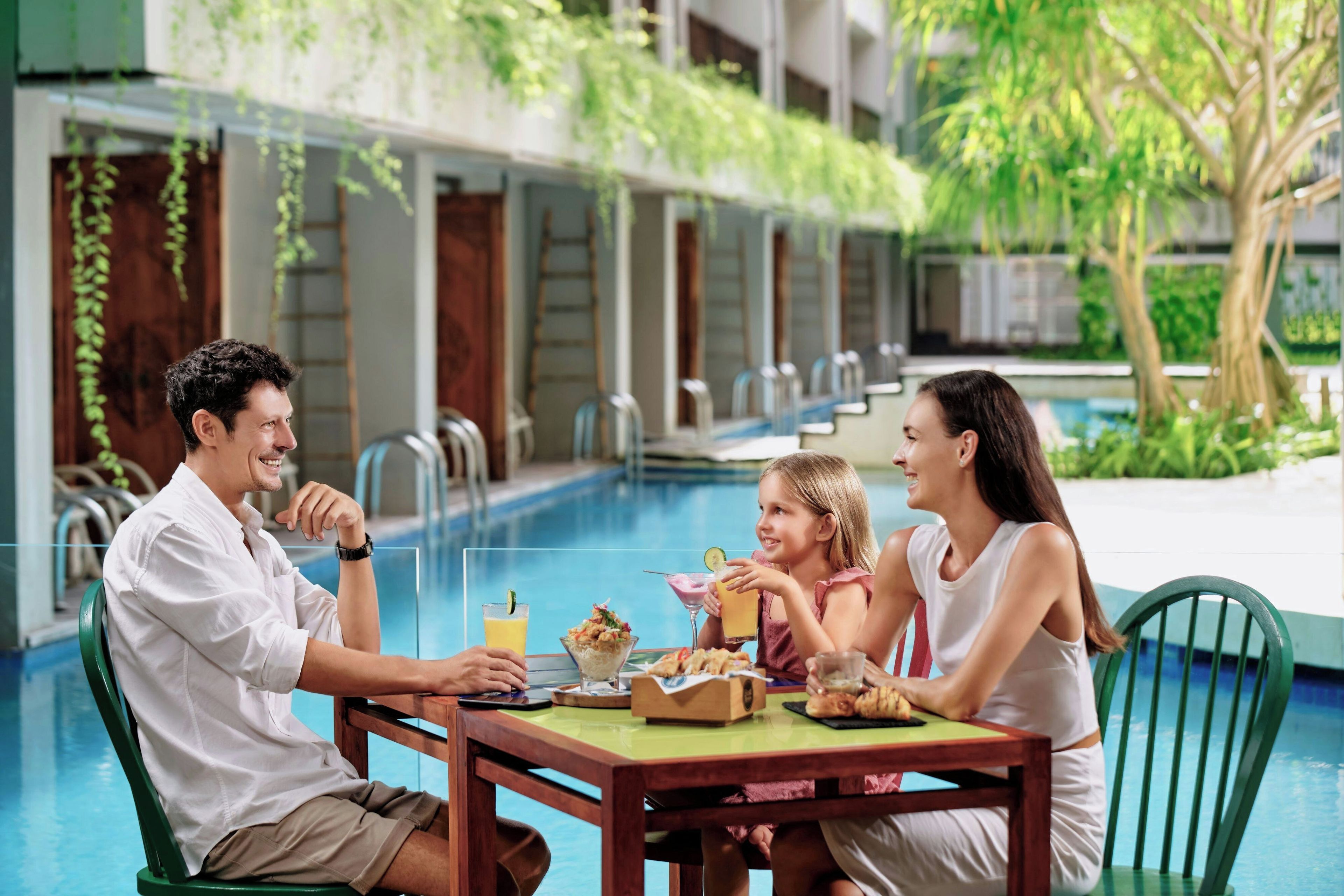 Un comedor con vista a la piscina, una mesa con comida y bebidas, y un ambiente junto a la piscina.