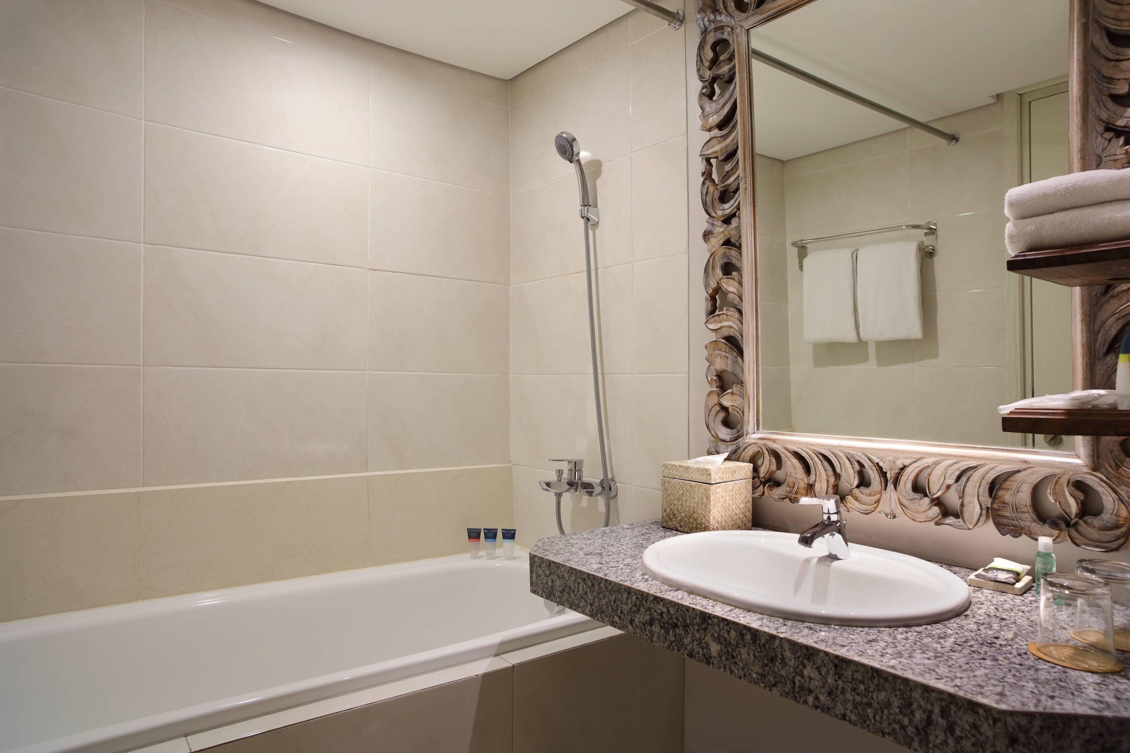 A bathroom with a bathtub, a sink, and a large mirror with ornate detailing.