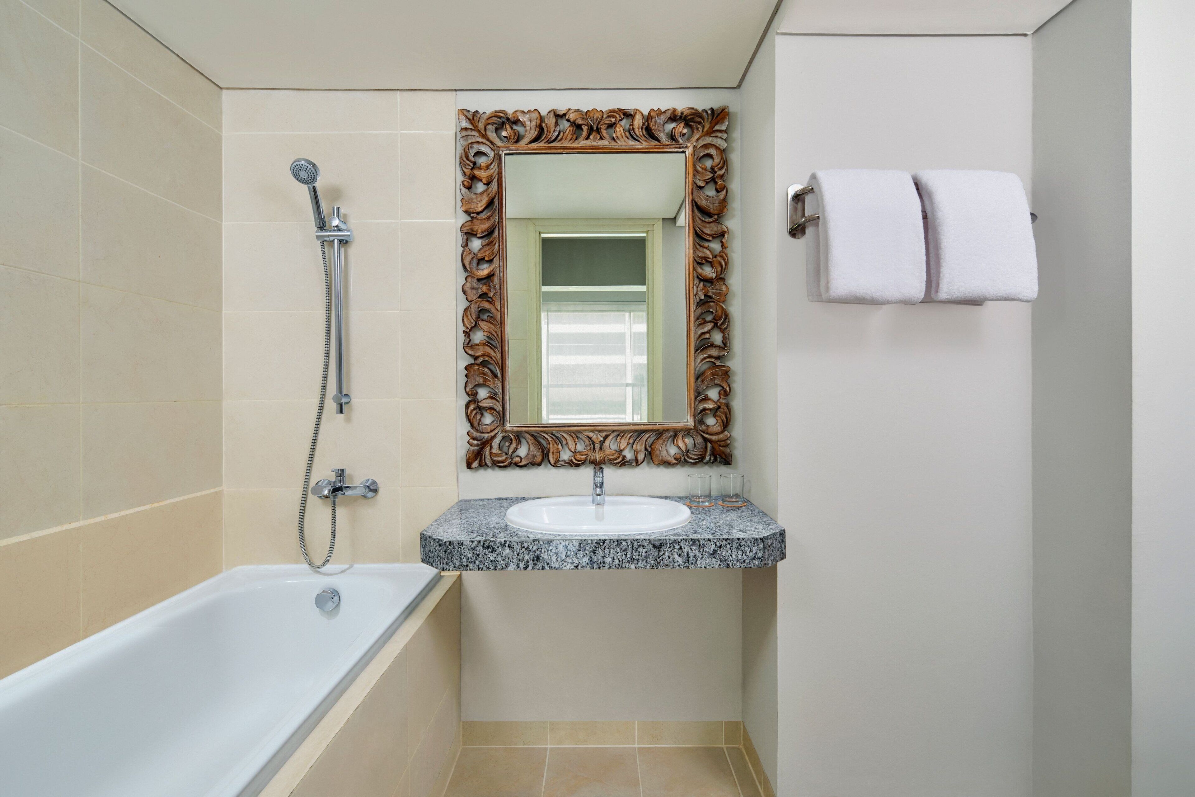 A bathroom with a bathtub, a sink with a marble countertop, a large ornate mirror, and two towels hanging on a towel rack.