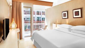 A hotel room with a large bed, a TV, a lamp, and a view of a balcony with a railing.