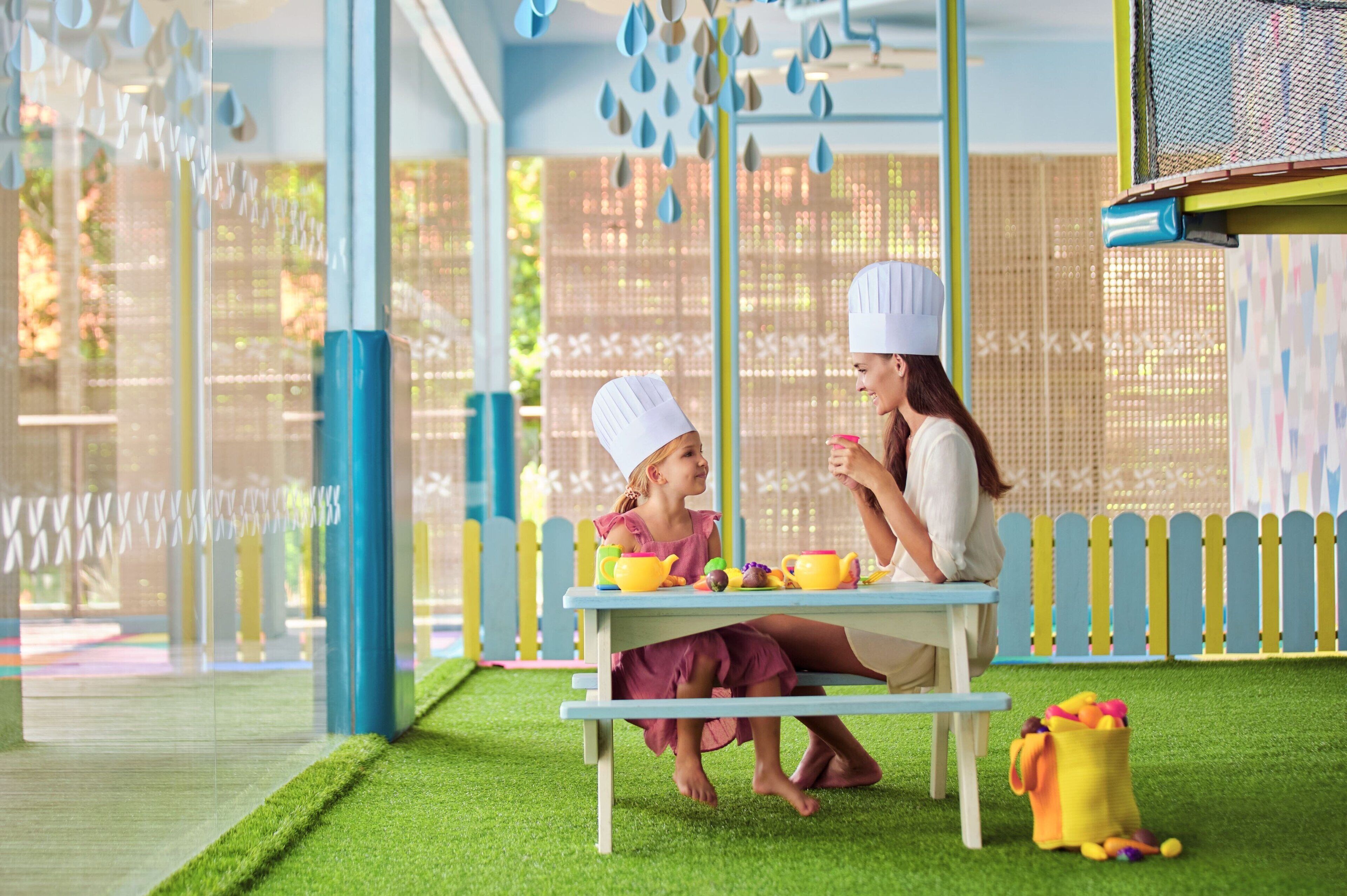 A child and an adult sitting at a table with a toy kitchen set.