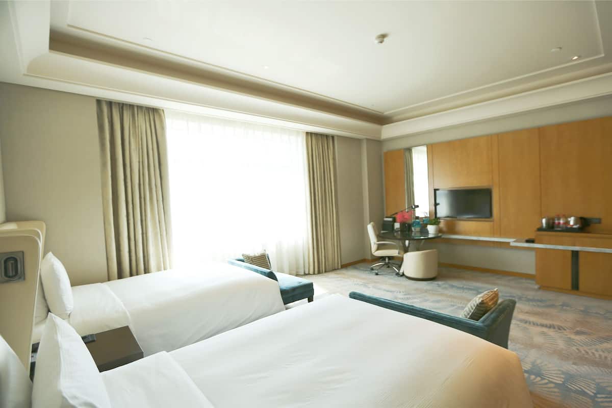 Habitación de hotel con dos camas, un escritorio con televisor y un ventanal con cortinas.