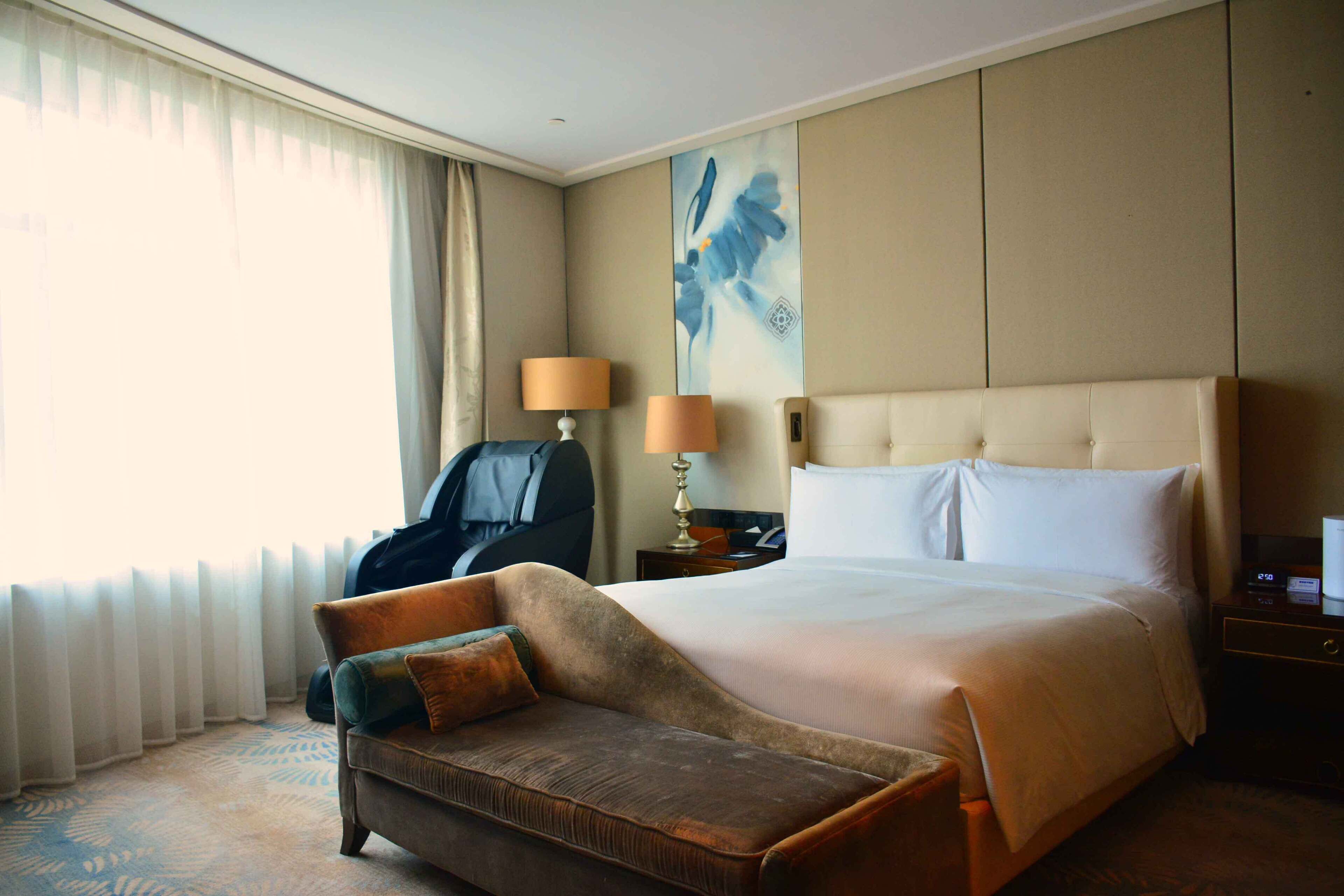 A hotel room with a large bed, a sofa, a chair, a lamp, and a painting on the wall.