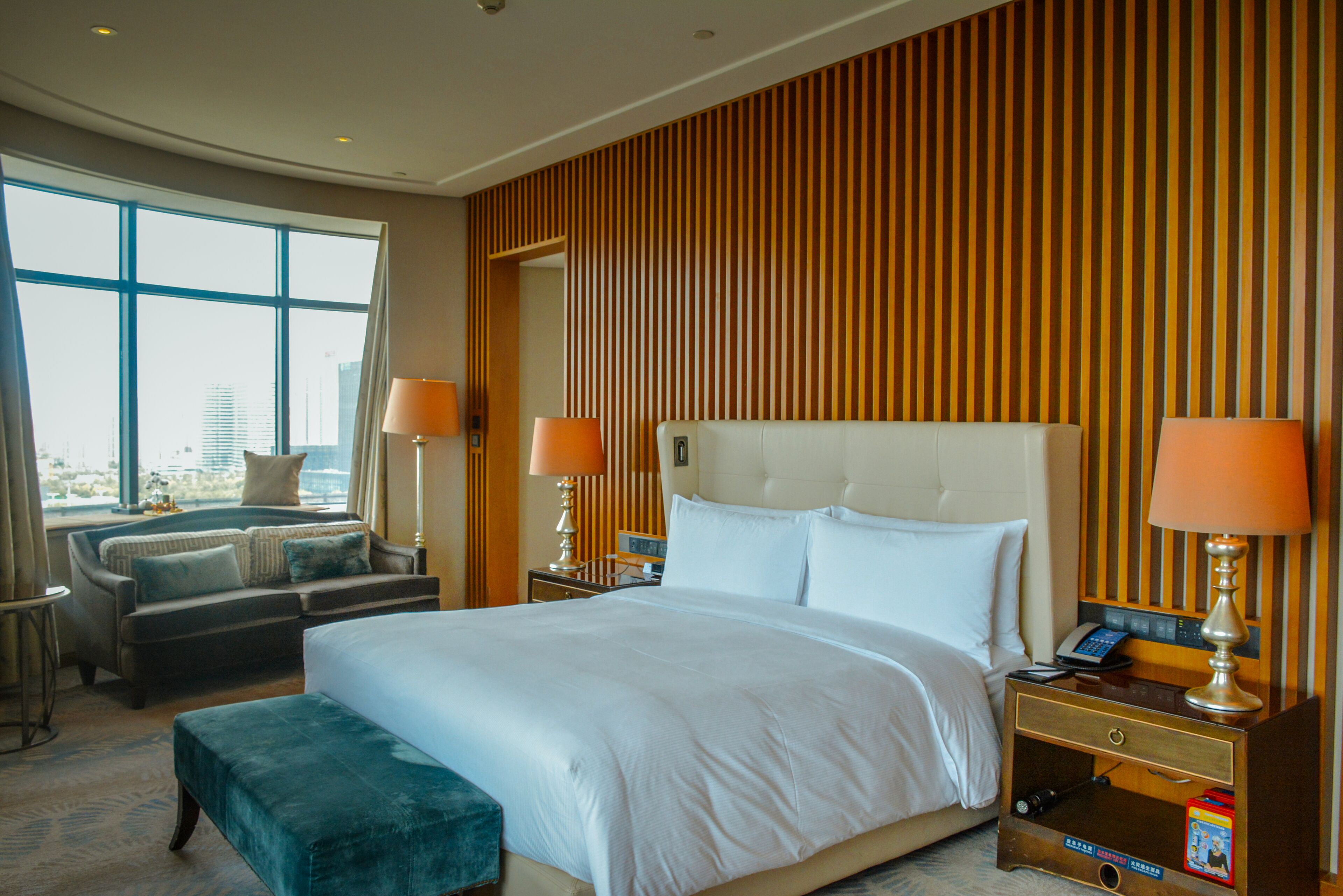 A hotel room with a large bed, two bedside tables with lamps, a sofa, and a view of the city.