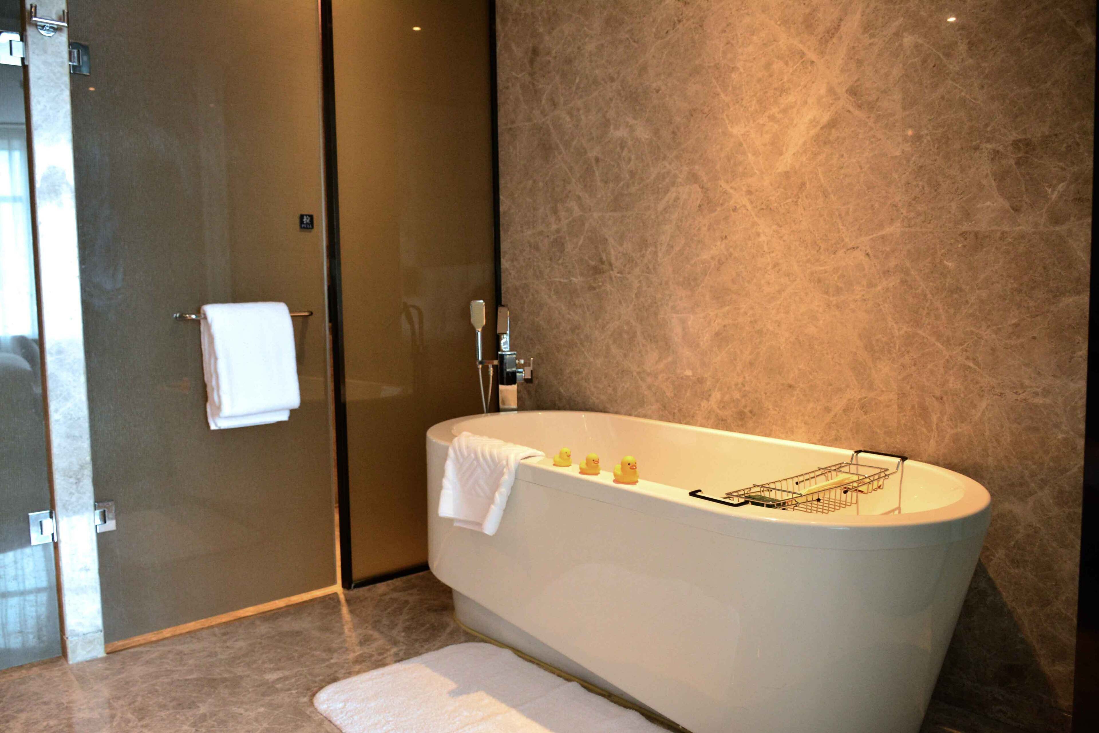 Un baño moderno con una bañera independiente, una cabina de ducha de vidrio y una pared de mármol.