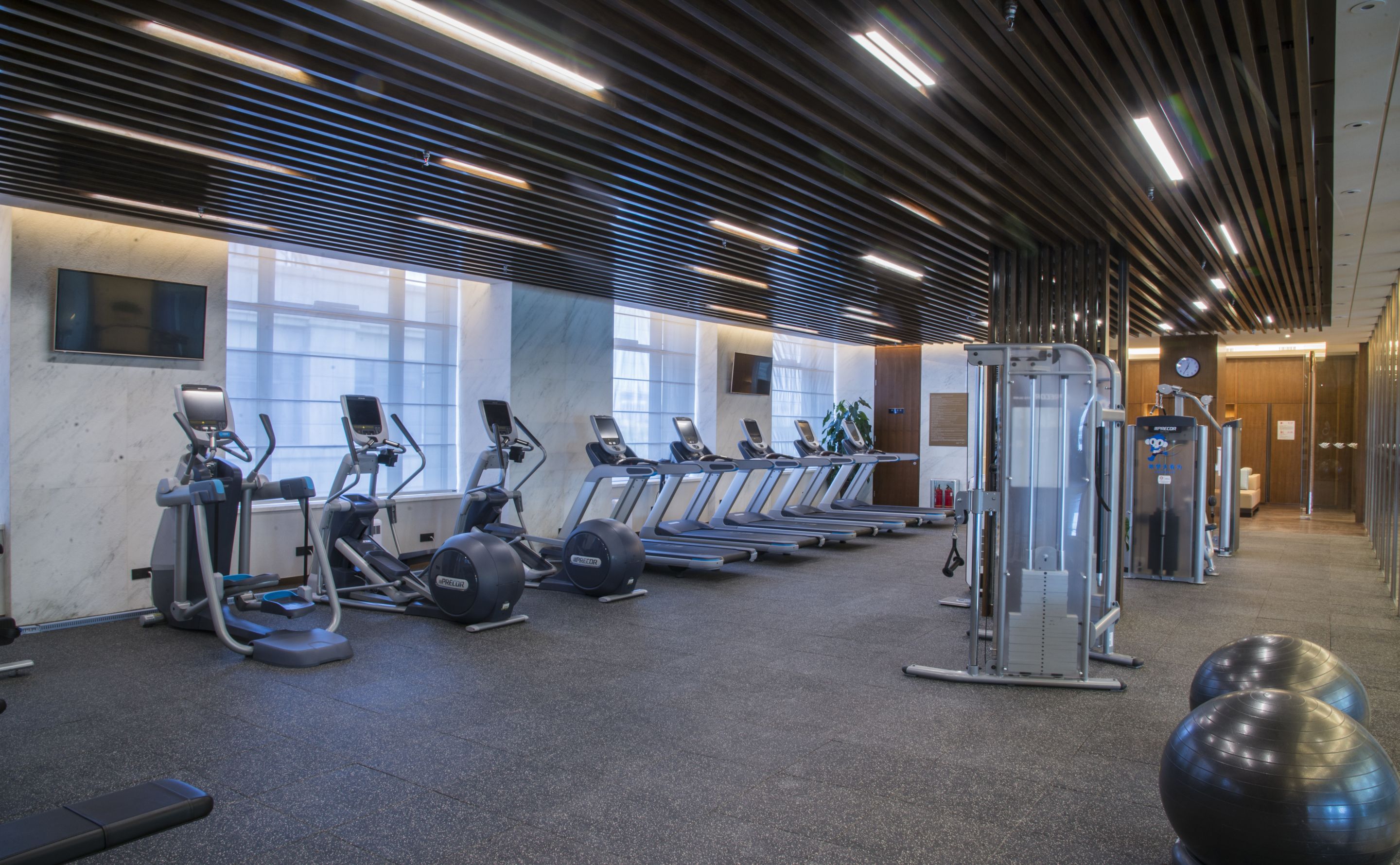 Une salle de sport équipée de tapis de course, de vélos elliptiques et de ballons d’exercice.