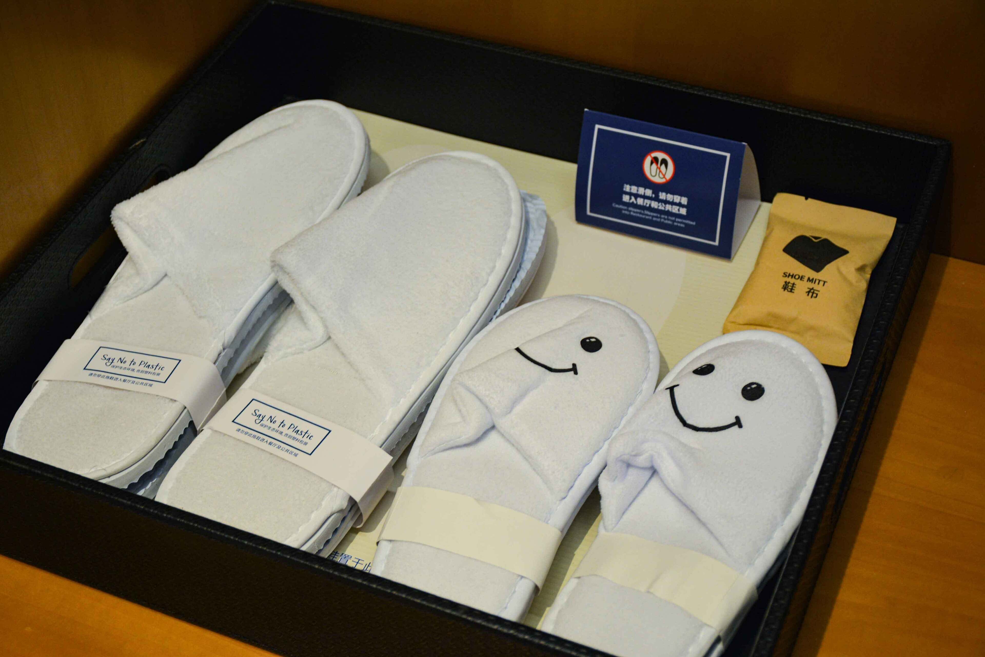 A box containing slippers with smiley faces, a shoe mitt, and a card with a no-smoking symbol.