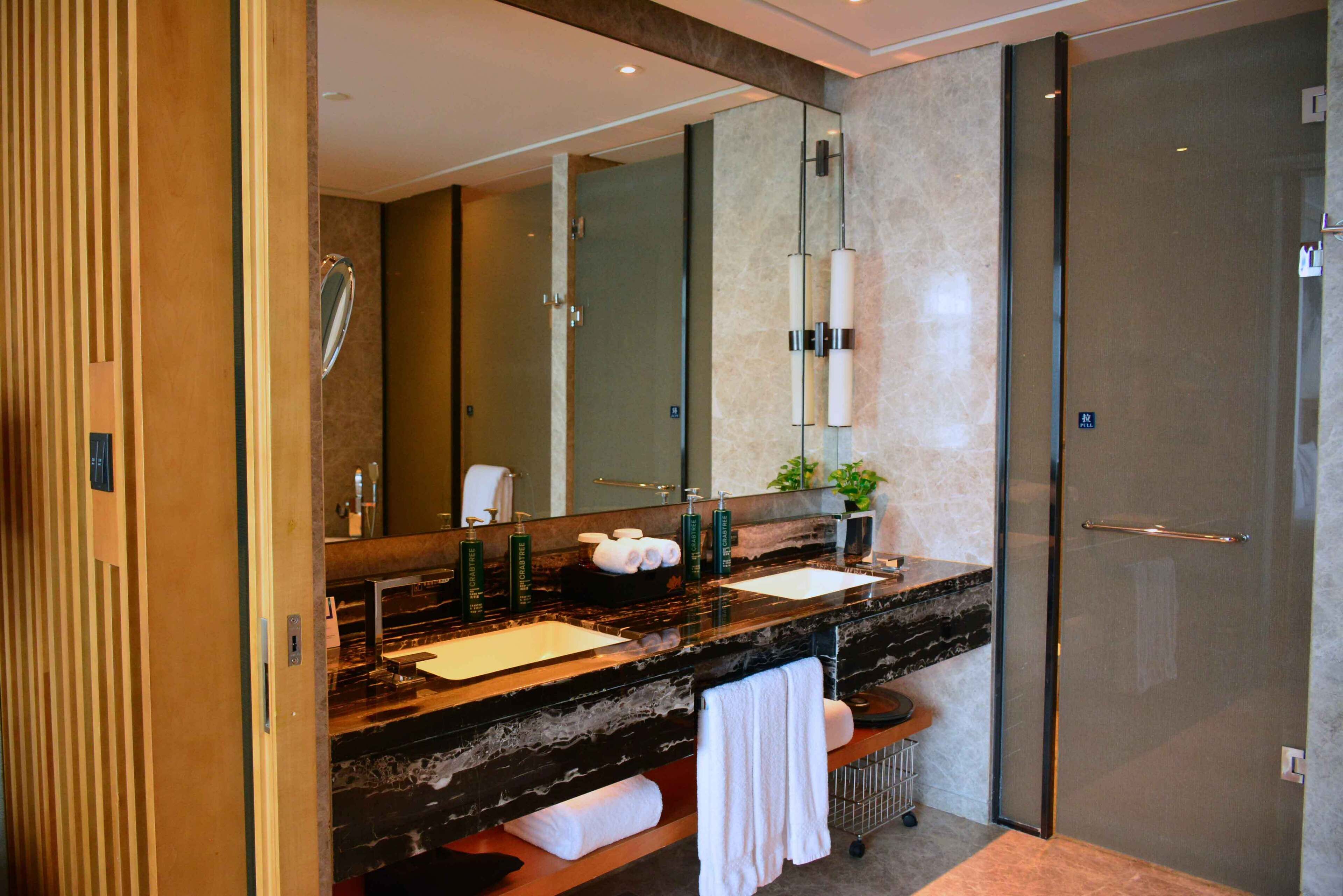 Une salle de bain moderne avec un meuble-lavabo en marbre, deux vasques, un grand miroir et une cabine de douche en verre.