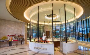 Un moderno vestíbulo de hotel con una isla central que presenta a un chef, un recinto de vidrio y un suelo de mármol.