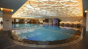 An indoor swimming pool with a geometric ceiling design, surrounded by lounge areas and a glass wall. - Hilton Urumqi (Ürümqi)