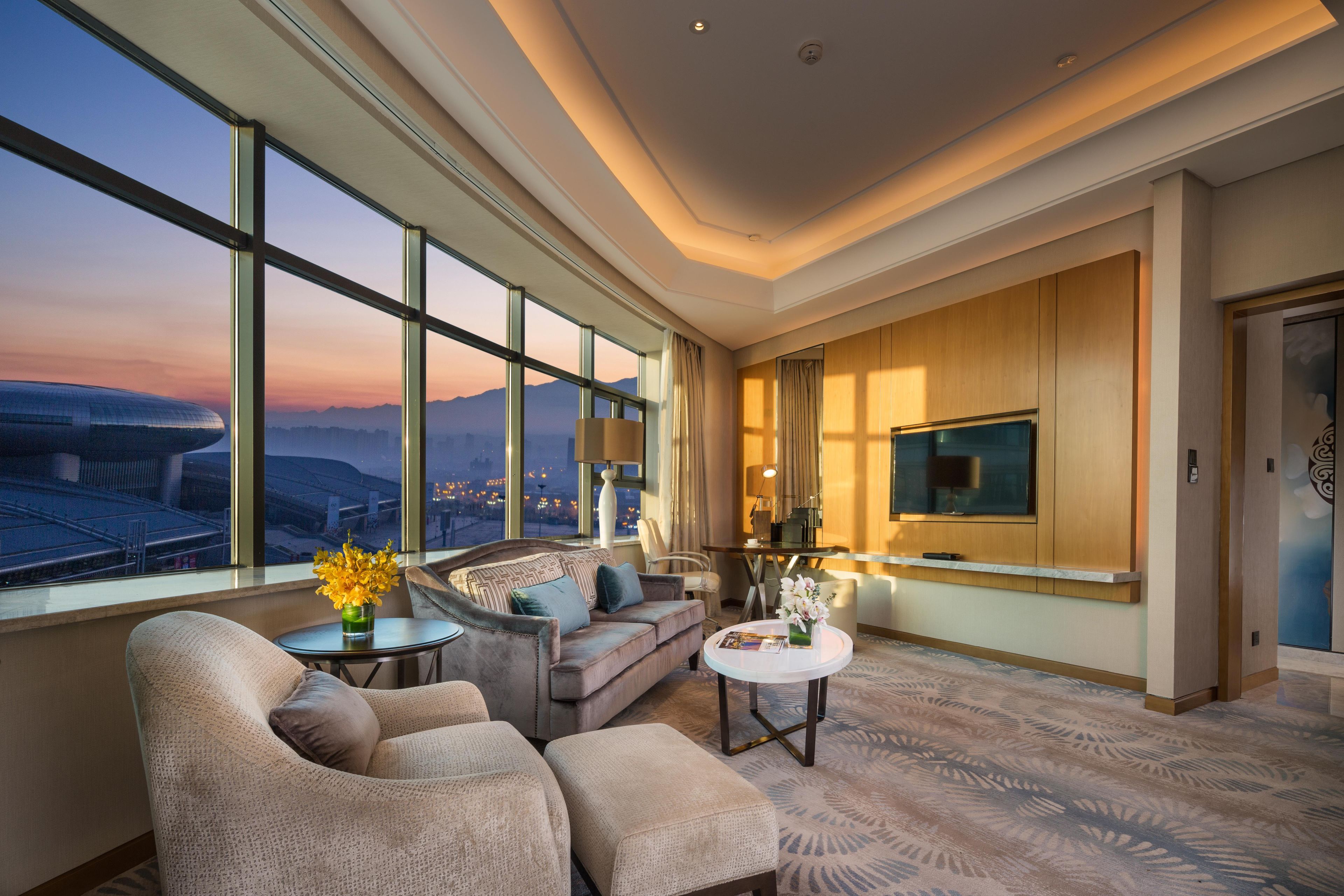 A modern living room with a large window, a sofa, a coffee table, and a flat-screen TV.