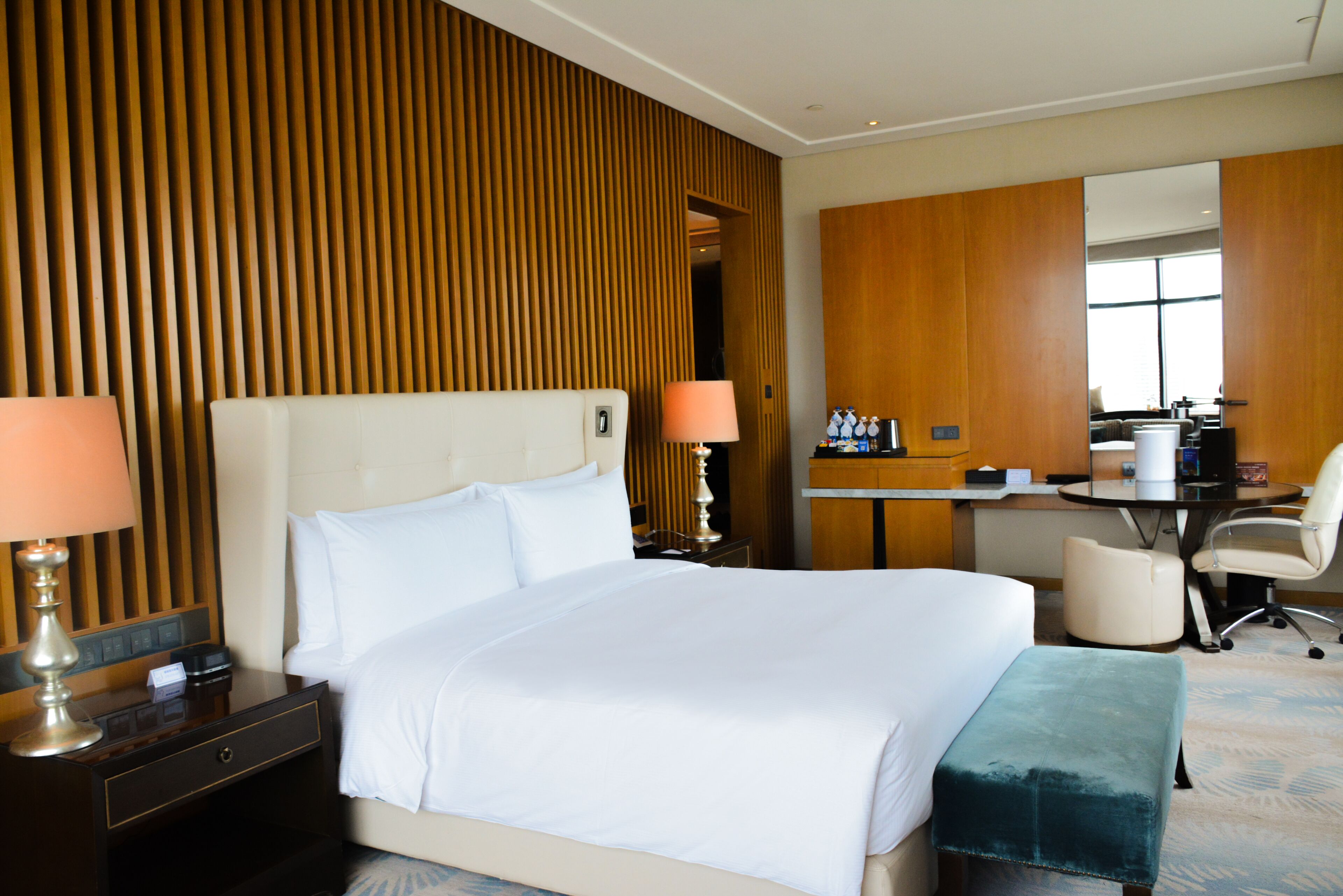 A hotel room with a large bed, bedside lamps, a desk with a chair, and a mirror.
