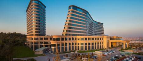 A modern hotel with two curved towers, a parking lot, and a view of the cityscape.