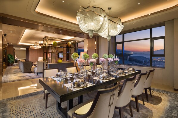 A modern dining area with a large island table, elegant chairs, and a view of the cityscape through large windows. - Hilton Urumqi (Ürümqi)