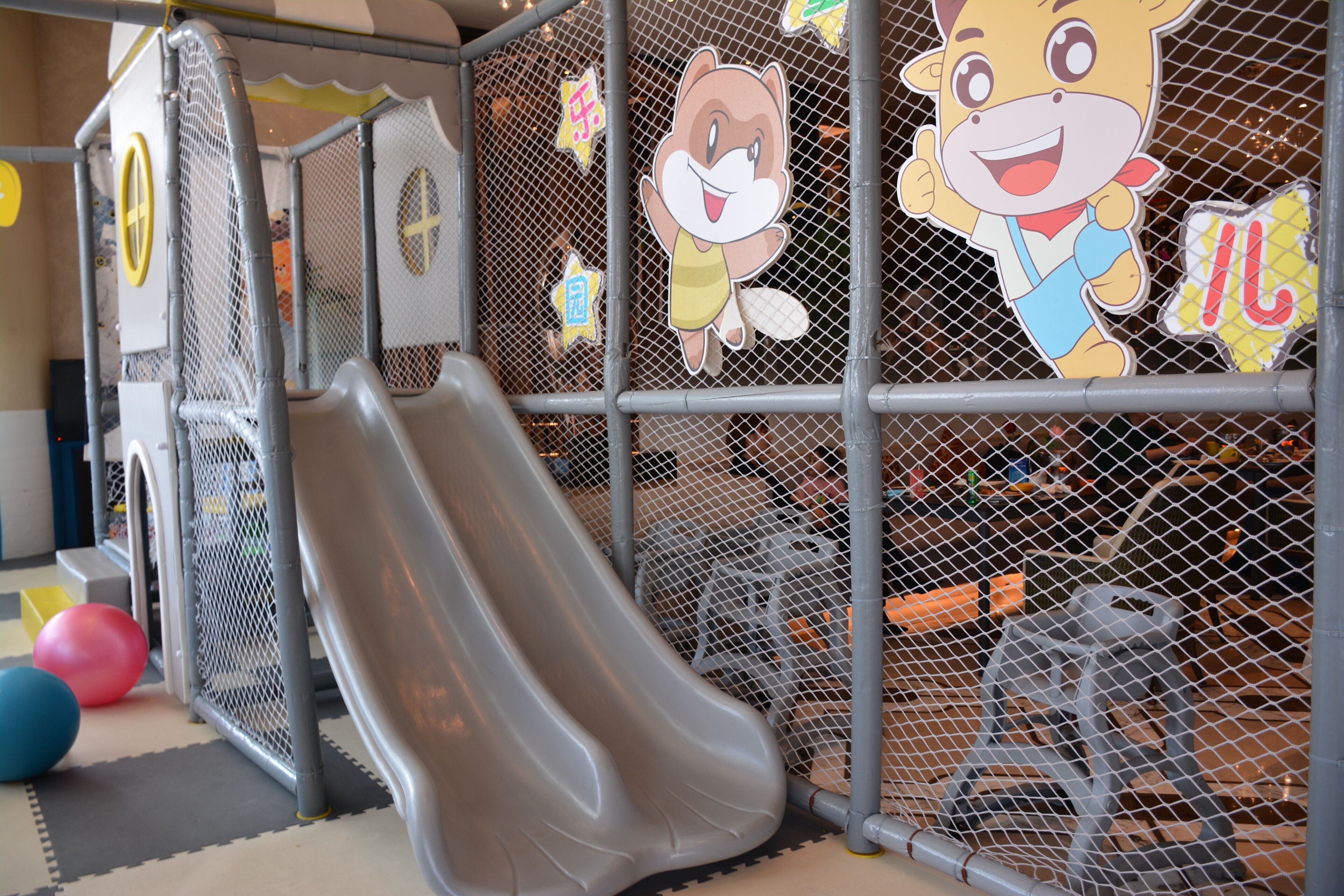 A children's play area with a slide, safety netting, and cartoon character decorations.